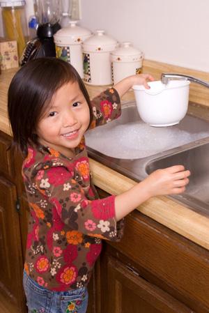 Маленька дівчинка миє посуд