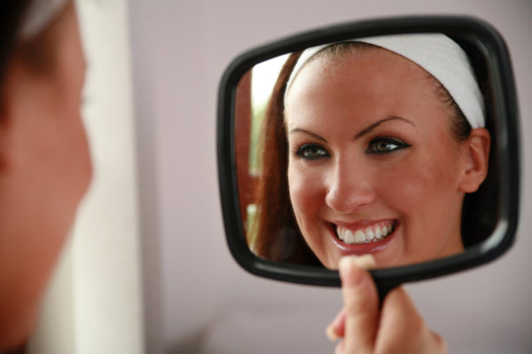 Женщина смотрит на зубы в зеркале