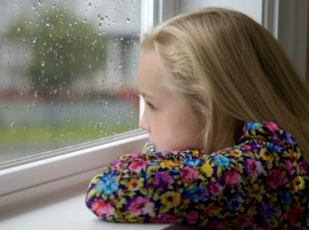 Znudzona dziewczyna wygląda przez okno w deszczowy dzień
