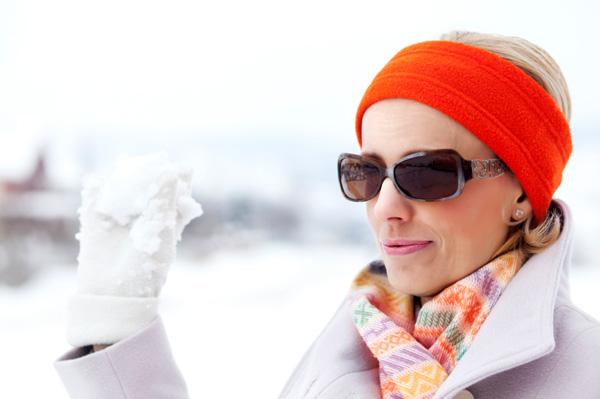 Nő napszemüveget visel, miközben játszik a hóban