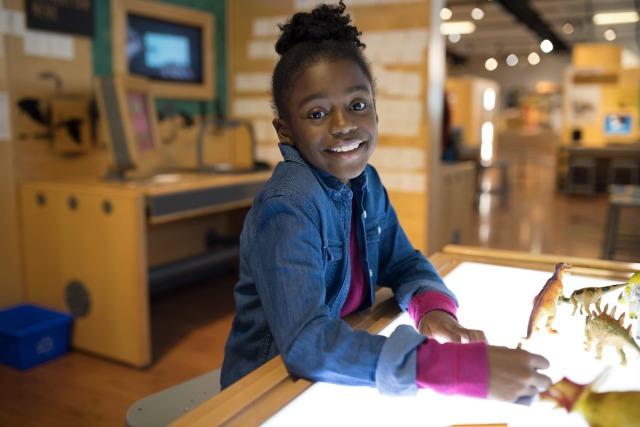 Mlado dekle se nasmehne, ko se igra s plastičnimi dinozavri v znanstvenem centru za dinozavre.
