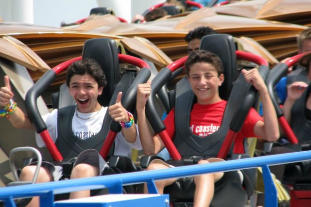 Anak-anak di kamp Thrill Coaster Tours tersenyum saat mereka menaiki rollercoaster.