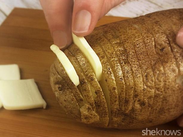 Butterfladen zwischen die Lamellen einer Hasselback-Kartoffel schieben