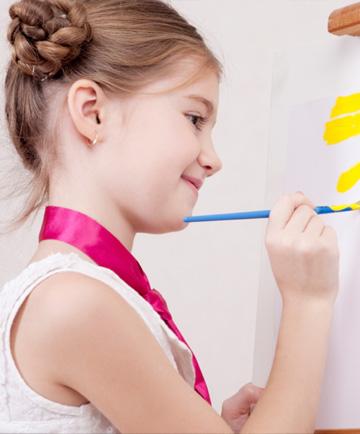 Маленька дівчинка малює на мольберті