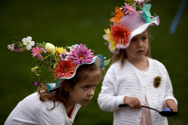 Dwie małe dziewczynki noszą ozdobne czapeczki wielkanocne podczas gry w jajko?