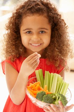 Маленька дівчинка їсть овочі